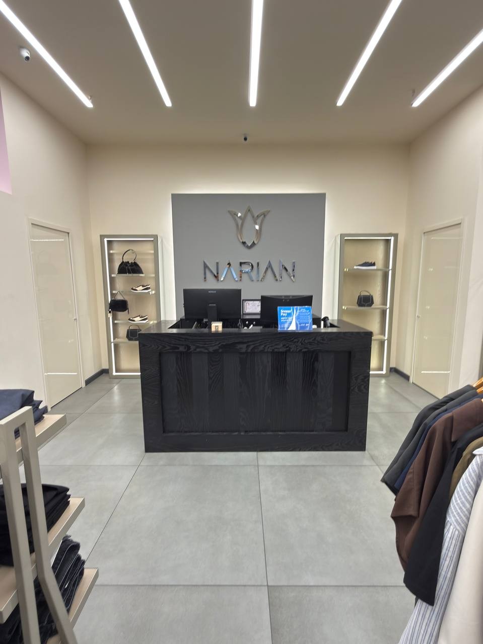 Photograph of the checkout counter in a Narian branch: a black counter in front of a grey wall with the Narian logo, lit shelves on both sides