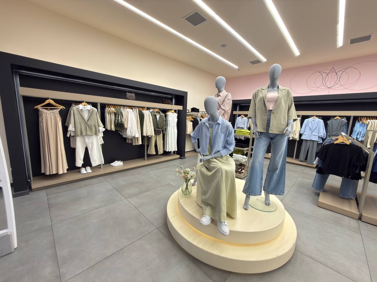 Photograph inside a Narian branch: three mannequins on a round cream platform in front of a pink wall with the tulip line drawing